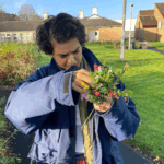 Priyanka is in a garden wearing a blue cost looking at some flowers that they have picked